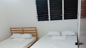 Dos camas individuales con cabeceros de madera, una ventana con persianas bajadas y suelo de baldosas.