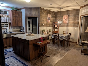 Una cocina con armarios de madera, encimera de granito, comedor con mantel a cuadros y mesa de madera.