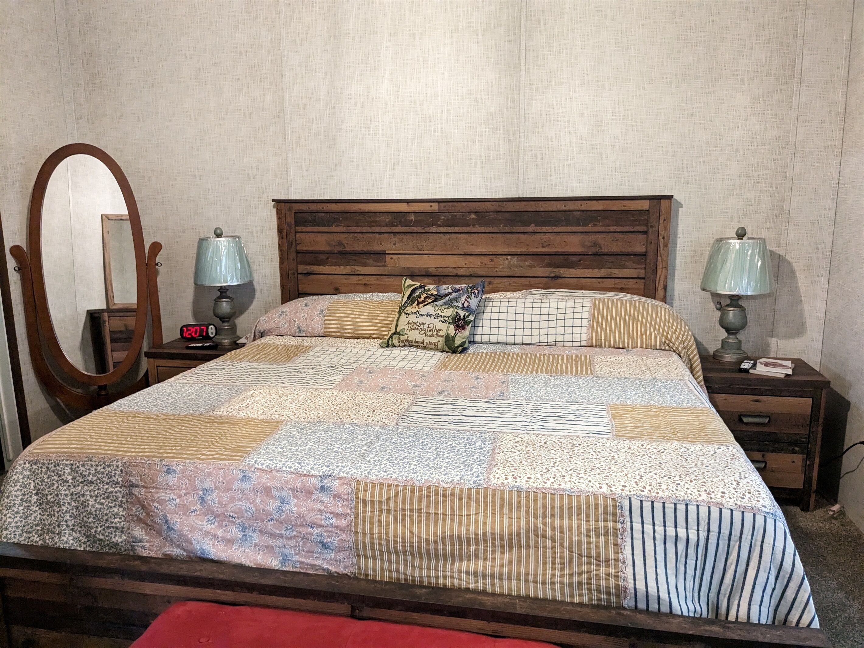 A bed with a quilt, two bedside tables with lamps, a mirror, and a clock.