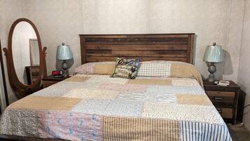 A bed with a quilt, two bedside tables with lamps, a mirror, and a clock.