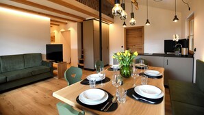 Een moderne eethoek met een houten tafel voor vier personen, een groene bank en een keuken op de achtergrond.