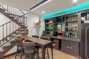 A bar area with stools, a mounted animal head, and shelves with bottles and glasses. - Lime Creek Retreat - Central Downtown (Rapid City)