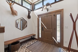 A foyer with a wooden bench, a mirror, a door, and two mounted animal heads. - Lime Creek Retreat - Central Downtown (Rapid City)