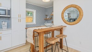A kitchen with white cabinets, a wooden table, bar stools, a round mirror, and a hanging light fixture.