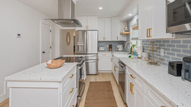 A modern kitchen with white cabinetry, stainless steel appliances, and a marble countertop.