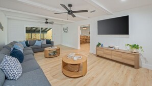 A modern living room with a grey sectional sofa, two round wooden coffee tables, a TV on the wall, and a wooden cabinet.
