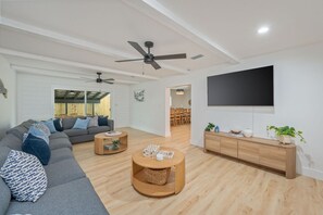 A modern living room with a grey sectional sofa, two round wooden coffee tables, a TV on the wall, and a wooden cabinet.