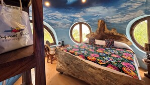 A bedroom with a bed, a ceiling fan, a round window, and a wall mural.