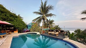 A swimming pool with lounge chairs, a palm tree, and a view of the ocean.