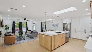 Una cocina moderna con una isla central, electrodomésticos de acero inoxidable y un comedor con sofá y mesa de centro.