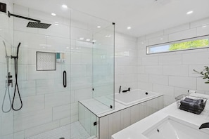 Een moderne badkamer met een douche met glazen wand, een vrijstaand bad en een wastafelmeubel met een wastafel en handdoekhouder.