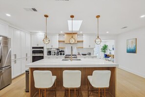 A modern kitchen with white cabinets, a central island with bar stools, and pendant lighting. - Dallas Home | Fire Pit · Spa Bath · Sleeps 11 (Dallas)