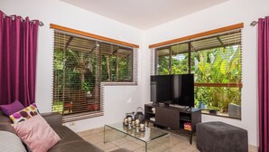 Una sala de estar moderna con sofá, reposapiés, mesa de centro de vidrio y televisor.