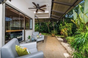 A covered patio with a ceiling fan, a gray sofa, a glass coffee table, and a variety of potted plants. - 3-bedroom villa in beautiful Quepos with AC for relaxing stays (Quepos)