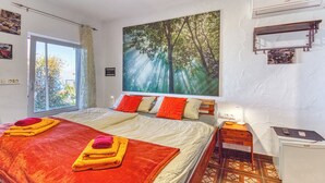 Un dormitorio con una cama grande, una mesita de noche, un escritorio y un cuadro de un bosque.