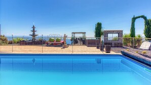 Una piscina con vista despejada al océano, una estructura de estilo pagoda y un área cercada con asientos.