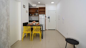 A compact kitchen with a refrigerator, a dining table with yellow chairs, and a small black table.