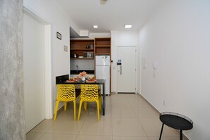 A compact kitchen with a refrigerator, a dining table with yellow chairs, and a small black table.