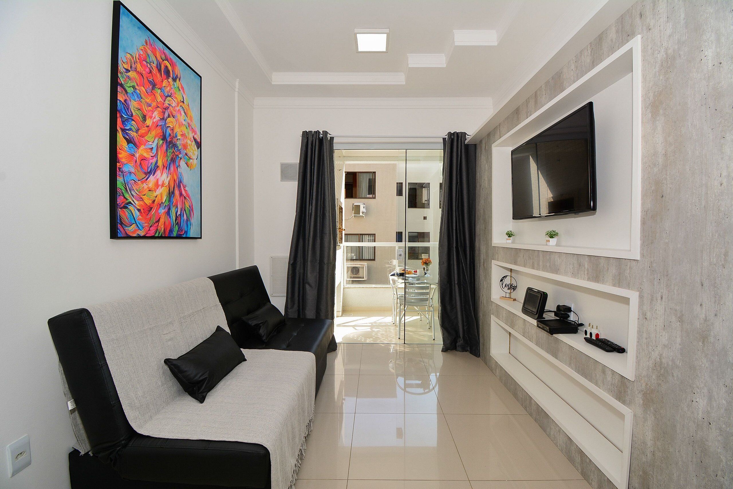 Una sala de estar moderna con un sofá, un televisor de pantalla plana, un cuadro y un comedor con una mesa de vidrio.