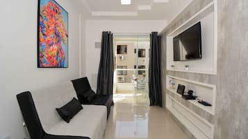 Una sala de estar moderna con un sofá, un televisor de pantalla plana, un cuadro y un comedor con una mesa de vidrio.