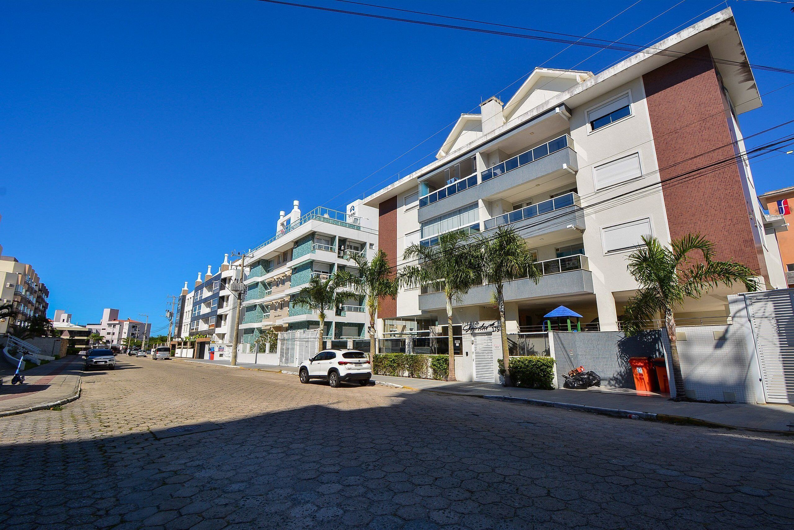 Un edificio residencial de varios pisos con balcones, una calle pavimentada y automóviles estacionados.