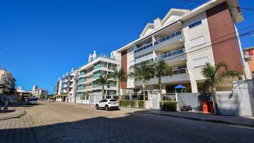 A multi-story residential building with balconies, a paved street, and parked cars.