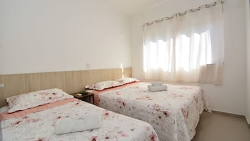 Habitación de hotel con dos camas, cabecero de madera, mesita de noche y ventana con cortinas.