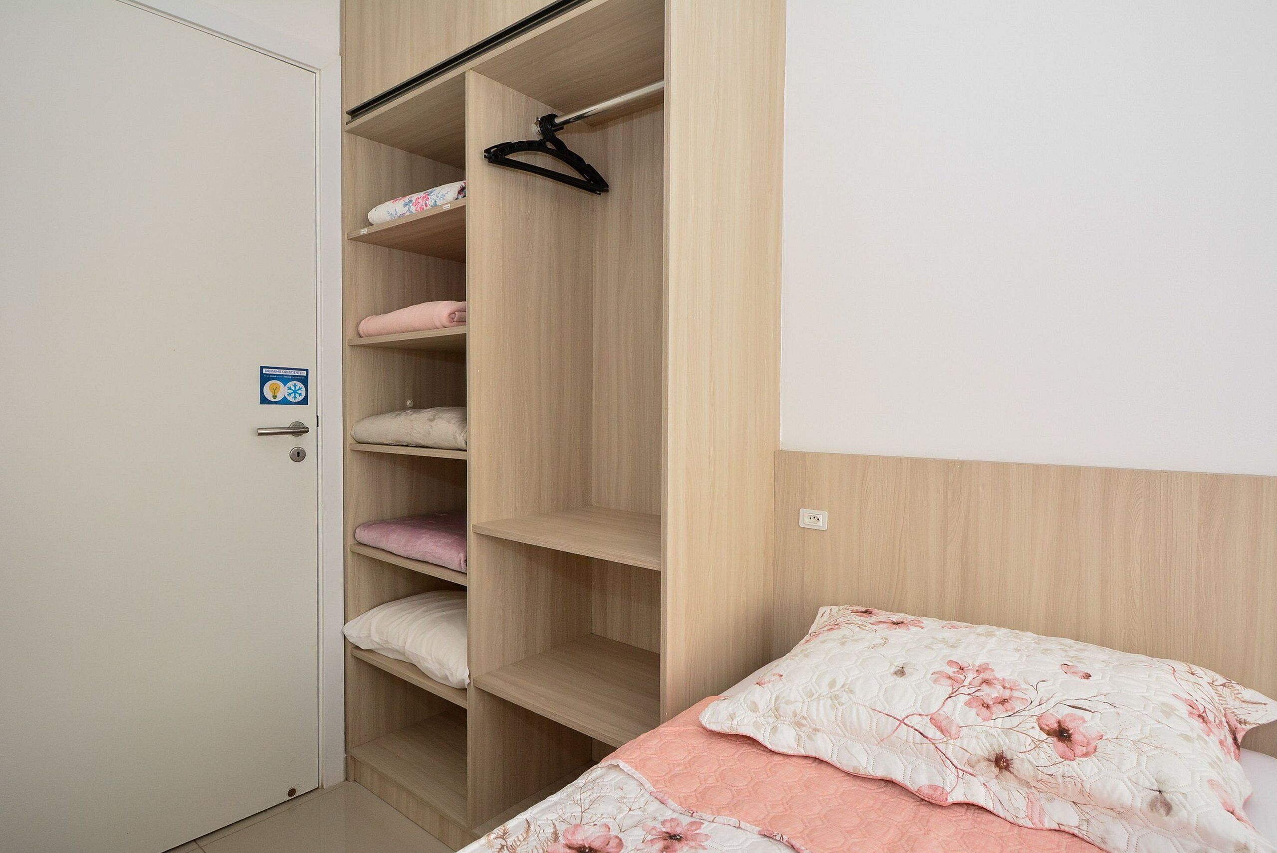 A bedroom with a bed, a wardrobe, and a hanging closet rod.