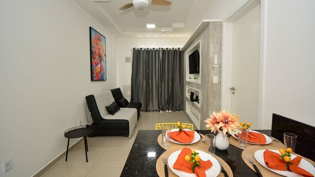 A dining area with a table set for four, a ceiling fan, a sofa, and a TV in the background.