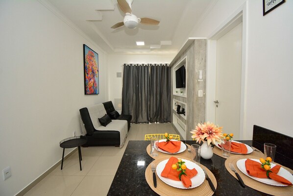 A dining area with a table set for four, a ceiling fan, a sofa, and a TV in the background.