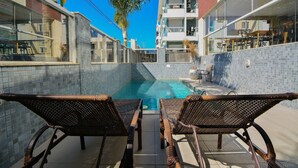 A poolside area with wicker chairs, a small pool, and a building with balconies.