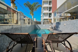 A poolside area with wicker chairs, a small pool, and a building with balconies. - Refúgio nos Ingleses a 200m da praia  (Florianópolis)