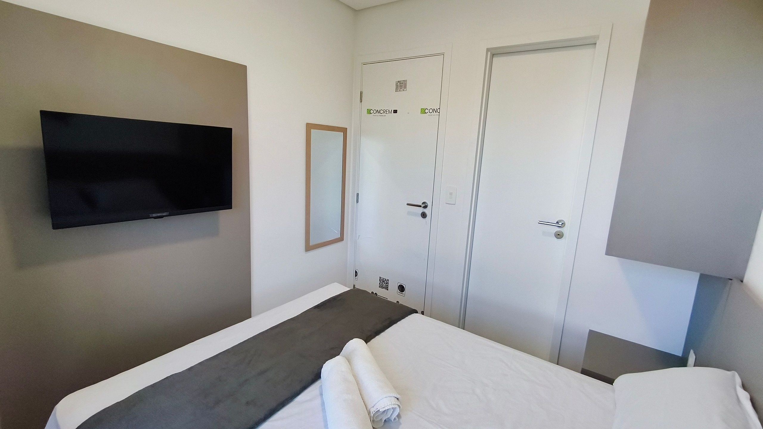 A hotel room with a bed, a TV mounted on the wall, and a door with a QR code.