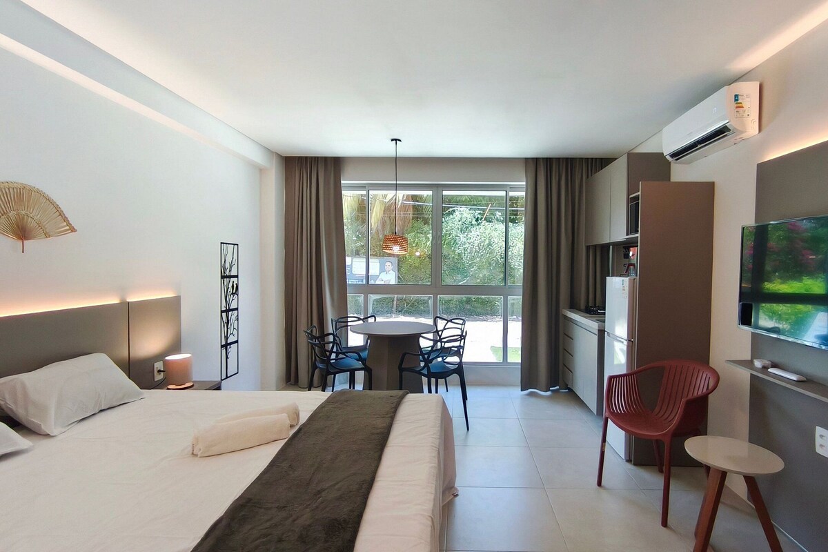 Ein Hotelzimmer mit einem Bett, einem Fernseher, einem Essbereich mit Stühlen und einem großen Fenster.