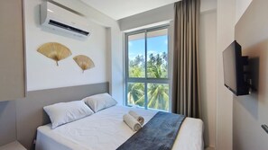 Ein Hotelzimmer mit Bett, Klimaanlage, zwei Wandventilatoren, einem großen Fenster mit Blick auf Palmen und einem Flachbildfernseher.