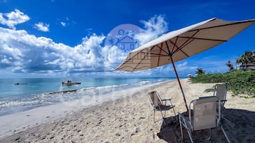 A beach with a large umbrella, two beach chairs, and a boat in the water.