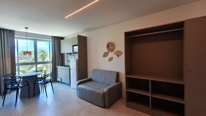 Ein modernes Wohnzimmer mit grauem Sofa, einem Essbereich mit Tisch und Stühlen, einer Küchenzeile und einem großen Kleiderschrank.