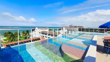 A rooftop infinity pool with a view of the ocean and palm trees.