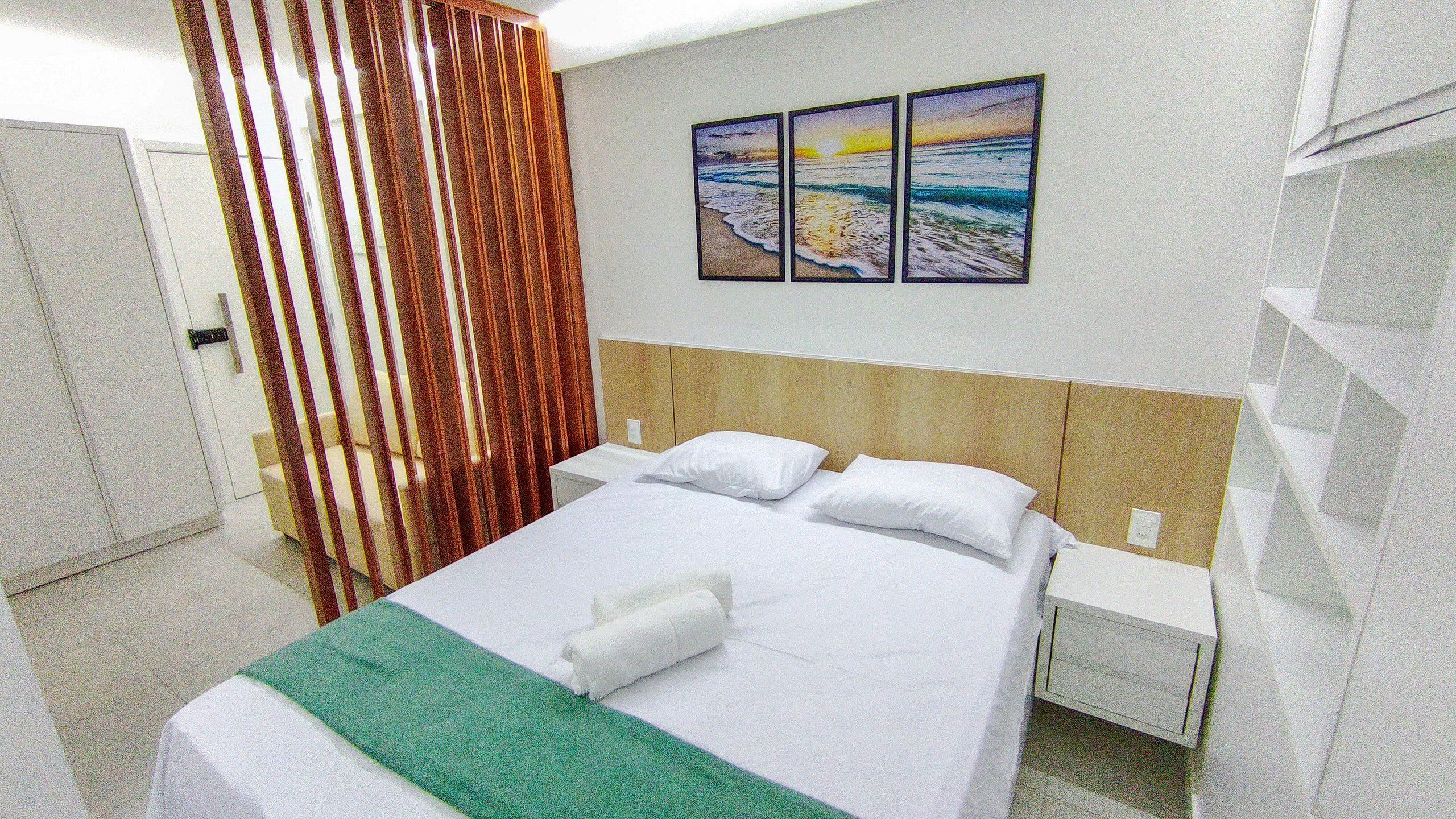 A hotel room with a bed, a nightstand, a wall-mounted painting, and a curtain.