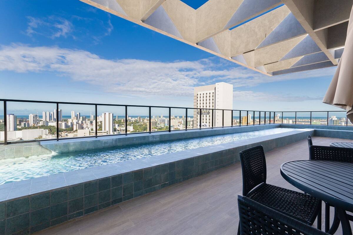 A rooftop pool with a city view, a table and chairs, and a modern ceiling design.