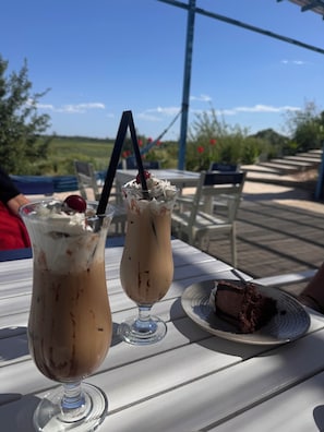 Dos cafés helados sobre una mesa blanca con una porción de pastel.