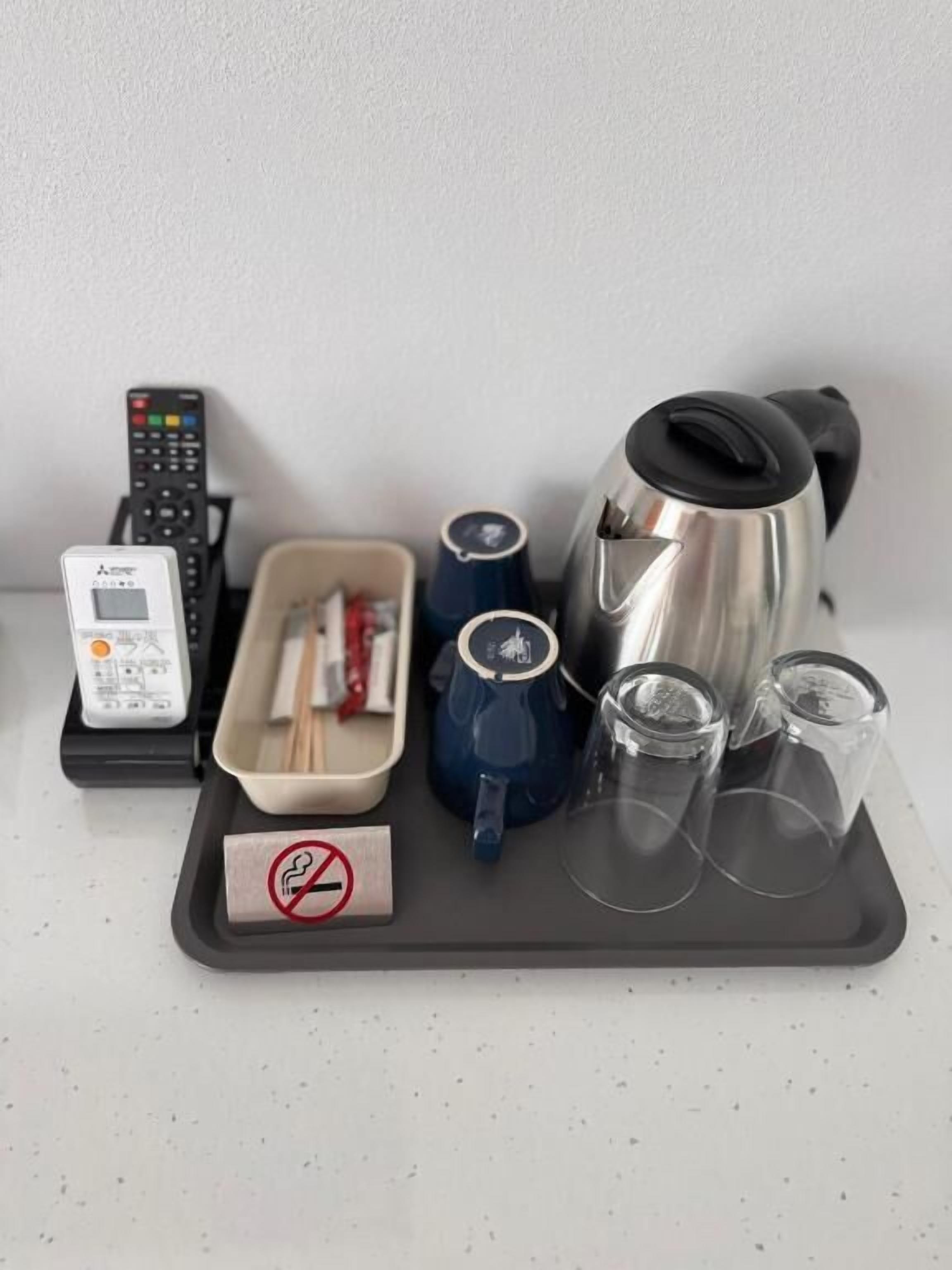 Ein Tablett mit einem Wasserkocher, Tassen, einer Fernbedienung, einem Telefon und einem Rauchverbot-Schild.