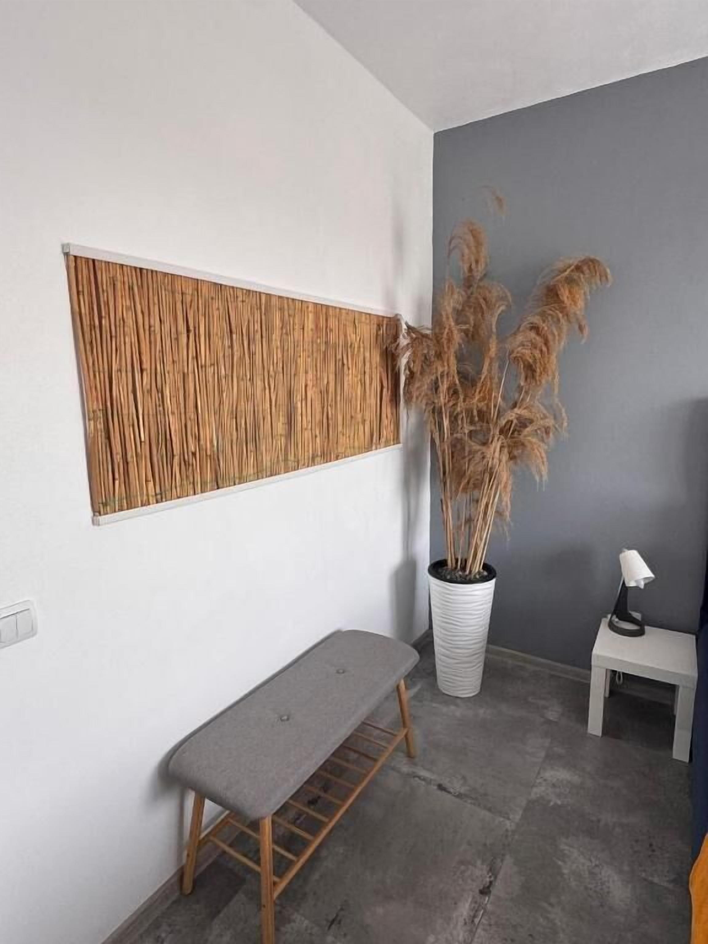 A room with a bench, a potted plant, a small table with a lamp, and a textured wall panel.