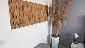 A room with a bench, a potted plant, a small table with a lamp, and a textured wall panel.