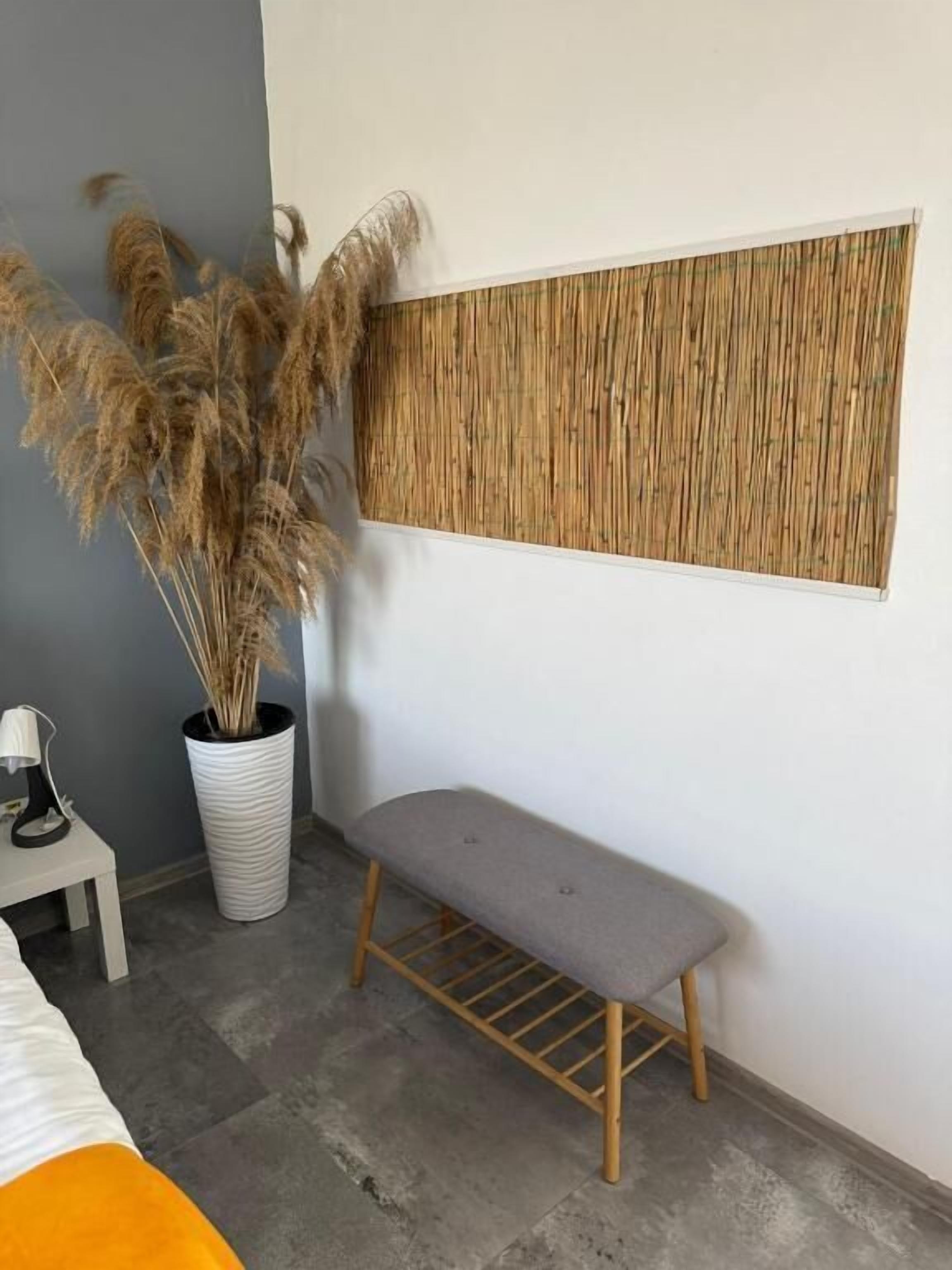 A room with a bench, a potted plant, a small table with a lamp, and a textured wall panel.