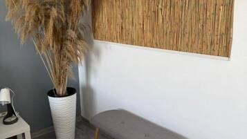 A room with a bench, a potted plant, a small table with a lamp, and a textured wall panel.