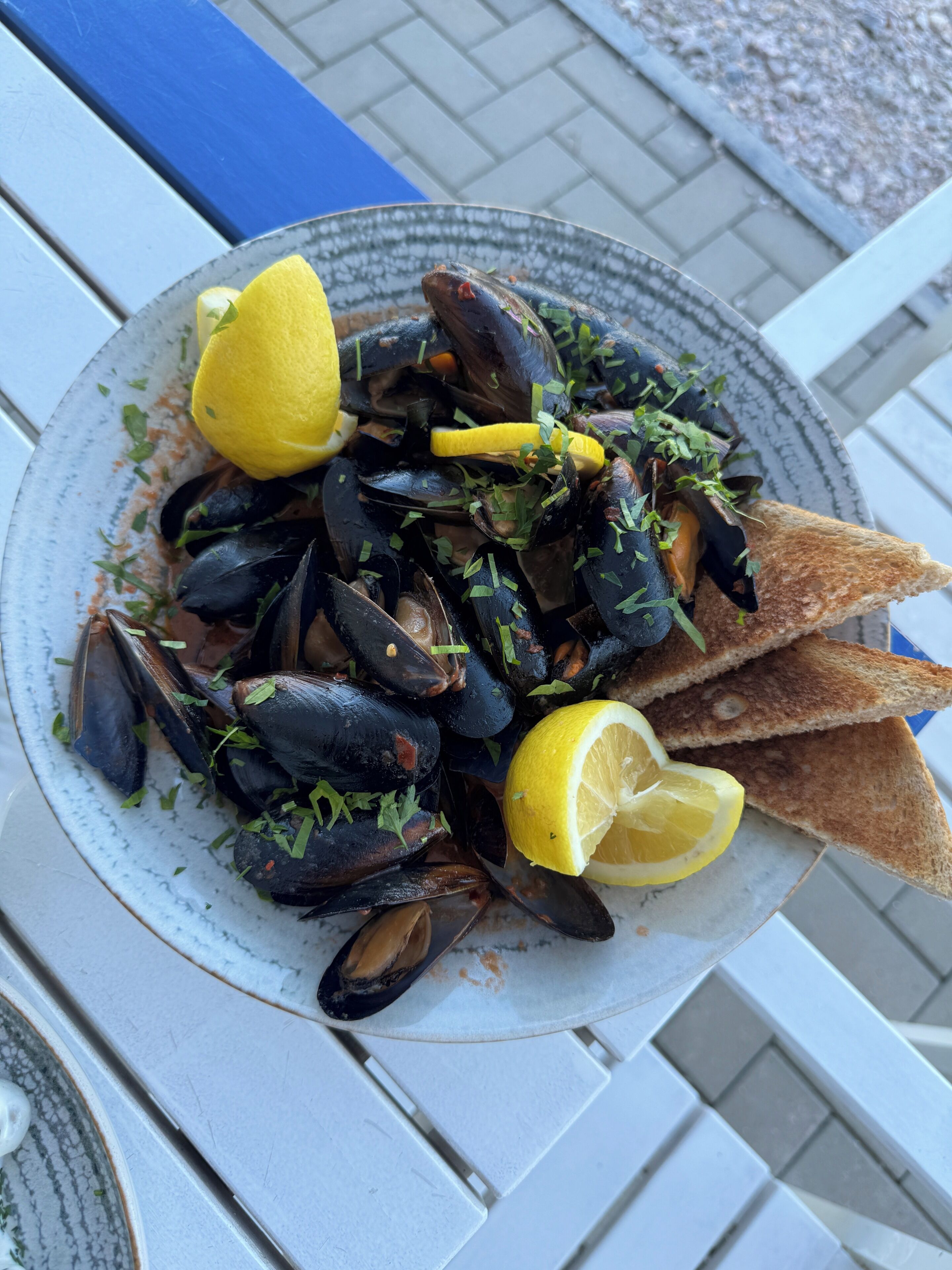 A plate of mussels with lemon wedges and chopped herbs, served on a white plate.