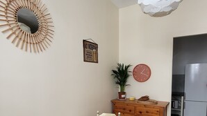 Ein Essbereich mit einem runden Tisch, Stühlen, einer an der Wand befestigten Uhr, einem dekorativen Spiegel und einer Pendelleuchte.