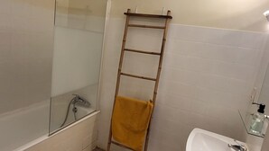Ein Badezimmer mit Duschkabine aus Glas, einem Holzhandtuchhalter, einem Waschbecken und einer Toilette.