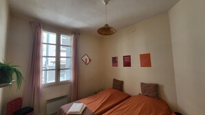 Ein Schlafzimmer mit Bett, einem fensterartigen Ausblick mit Vorhängen, einer Pendelleuchte und drei Wandbildern mit motivierenden Sprüchen.